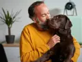 Hombre con barba besa a su perro chocolate. "No puedo seguir teniendo a mi perro, ¿qué hago?" se pregunta, abrazándolo.
