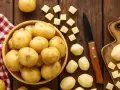 Patatas enteras y cortadas en cubos sobre una mesa de madera. ¡Un snack saludable que los perros pueden comer patata cocida!