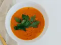 Un tazón de sopa de moro perros, decorado con perejil fresco y pimienta, junto a una cuchara dorada sobre tela.
