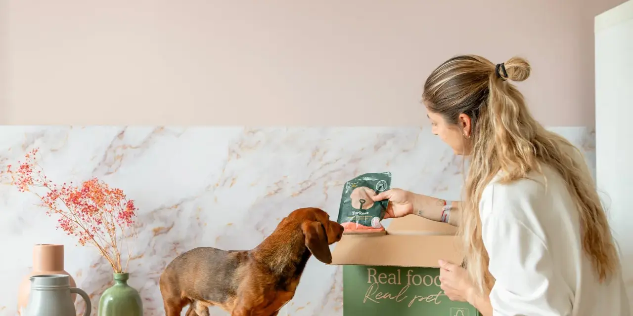 Una mujer le da a su teckel un paquete de comida para perros. Descubre qué dar de comer a un teckel con esta deliciosa opción.