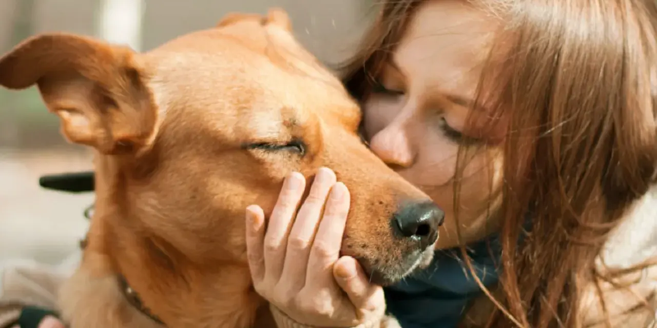 Una chica besa a su perro, que cierra los ojos, sintiendo el amor. Es la pura felicidad que siente un perro cuando le das un beso.