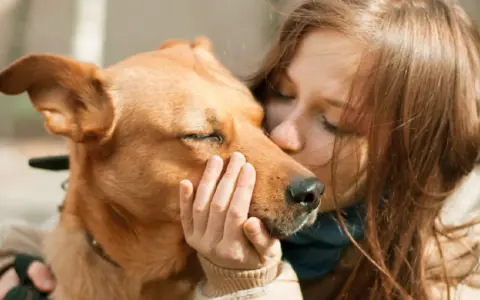 Una chica besa a su perro, que cierra los ojos, sintiendo el amor. Es la pura felicidad que siente un perro cuando le das un beso.