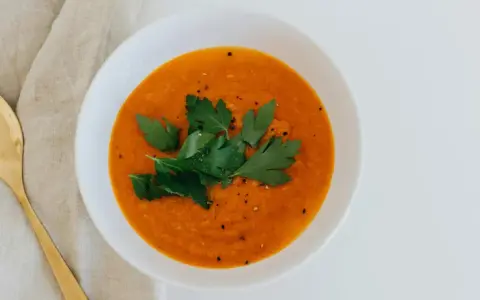 Un tazón de sopa de moro perros, decorado con perejil fresco y pimienta, junto a una cuchara dorada sobre tela.