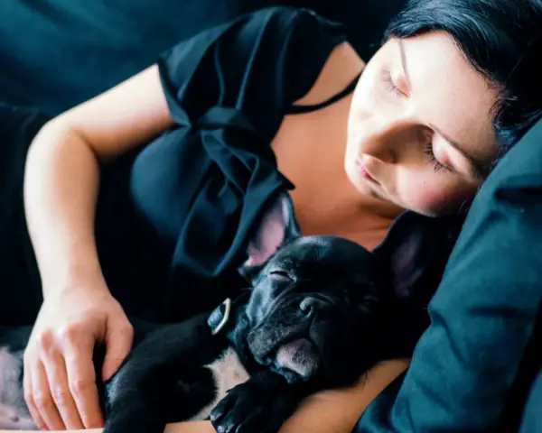 Una mujer duerme con su cachorro de bulldog francés negro. Mi perro se tumba a mi lado, ambos en un abrazo tierno y reconfortante.