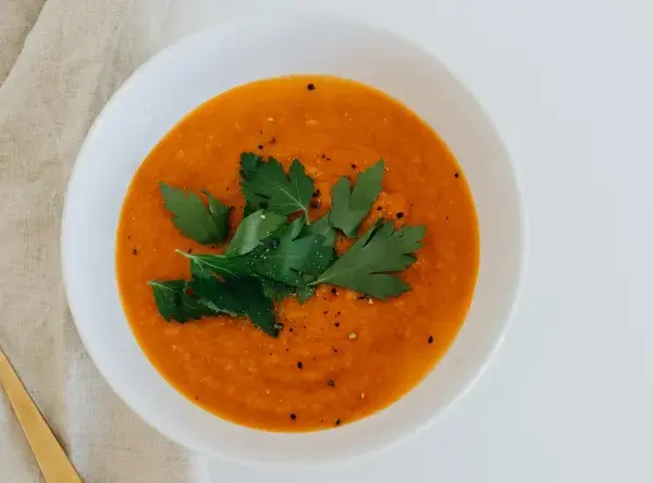 Un tazón de sopa de moro perros, decorado con perejil fresco y pimienta, junto a una cuchara dorada sobre tela.