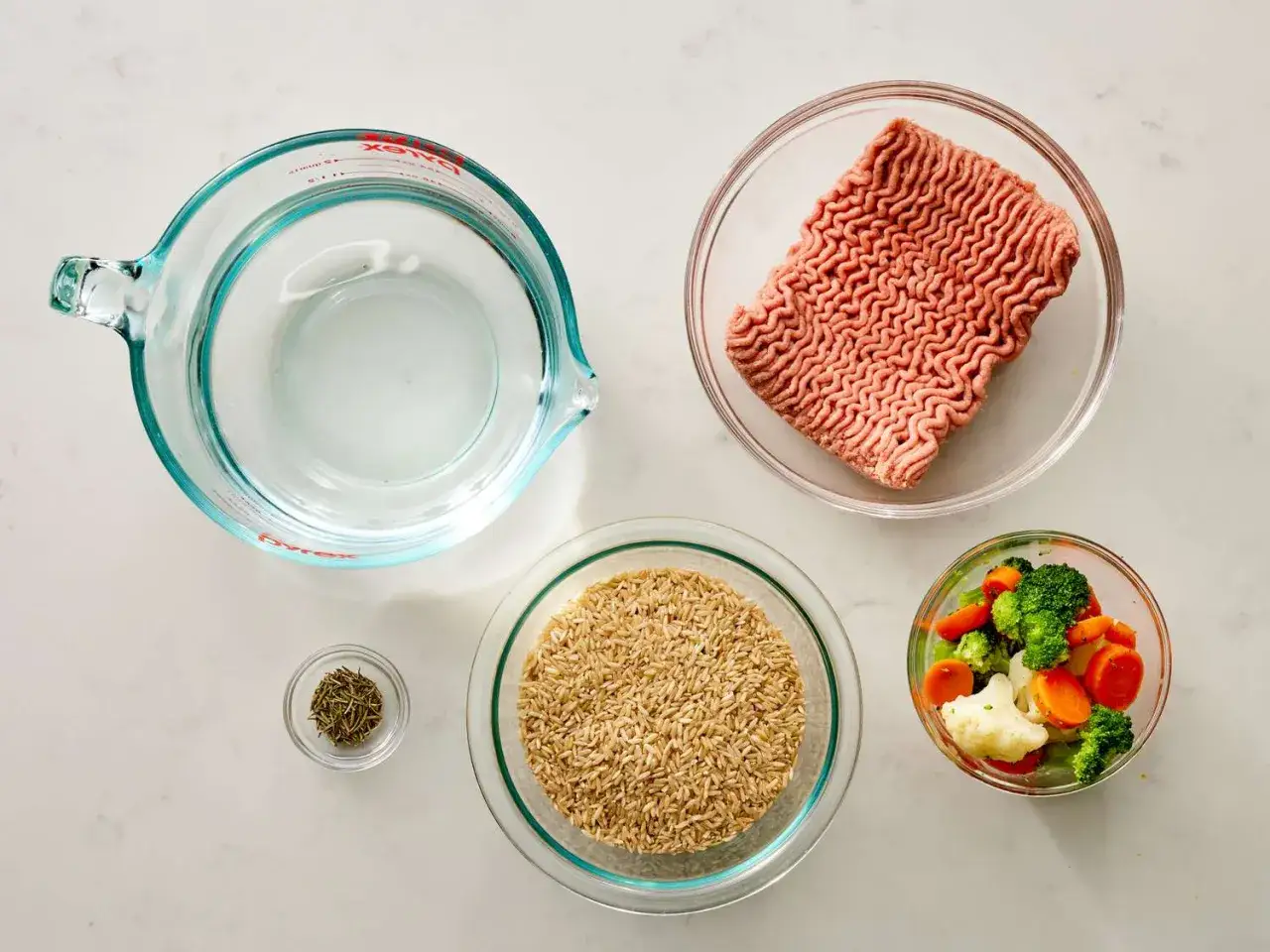 Ingredientes para comida casera para perros: carne picada, arroz integral, verduras mixtas, hierbas y agua.