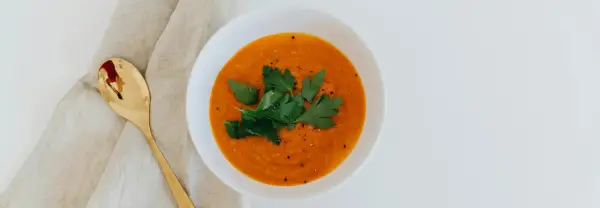 Un tazón de sopa de moro perros, decorado con perejil fresco y pimienta, junto a una cuchara dorada sobre tela.